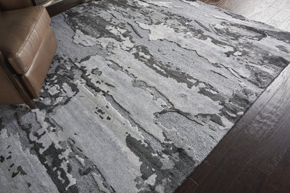 Abstract gray area rug with light and dark charcoal blotches on dark wood floor; brown leather recliner edge visible.