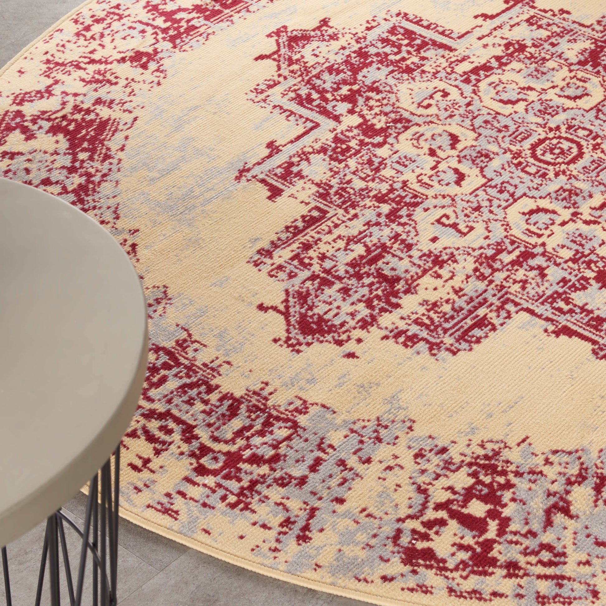Round beige distressed oriental rug with red medallion pattern and pale blue accents under a white round table.