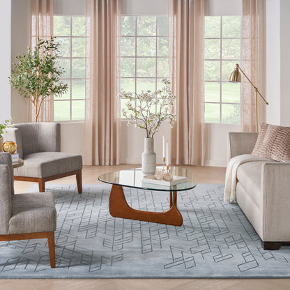 Contemporary living room with gray sofas & light blue geometric rug, glass coffee table with wooden base & beige curtains.