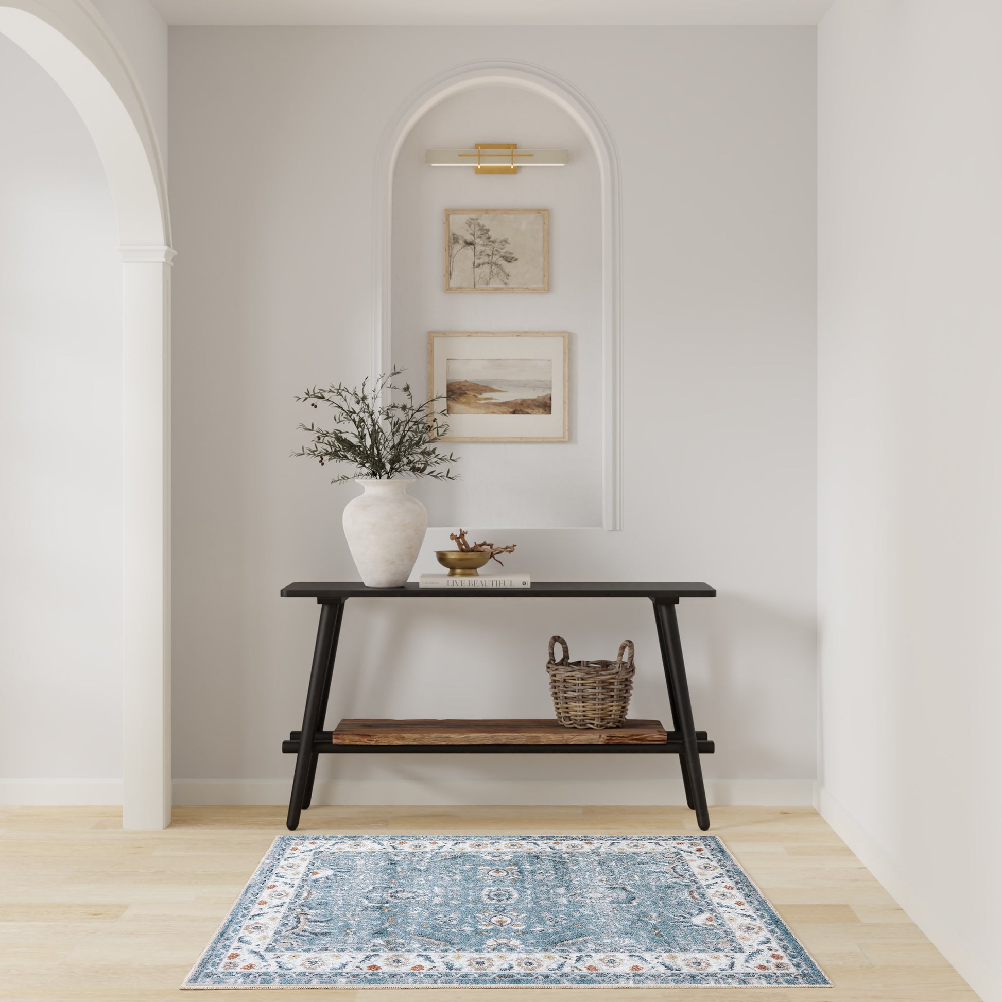 Black wooden console table with two tiers in a white arched entry, vase of greenery, basket, framed art & a blue rug.