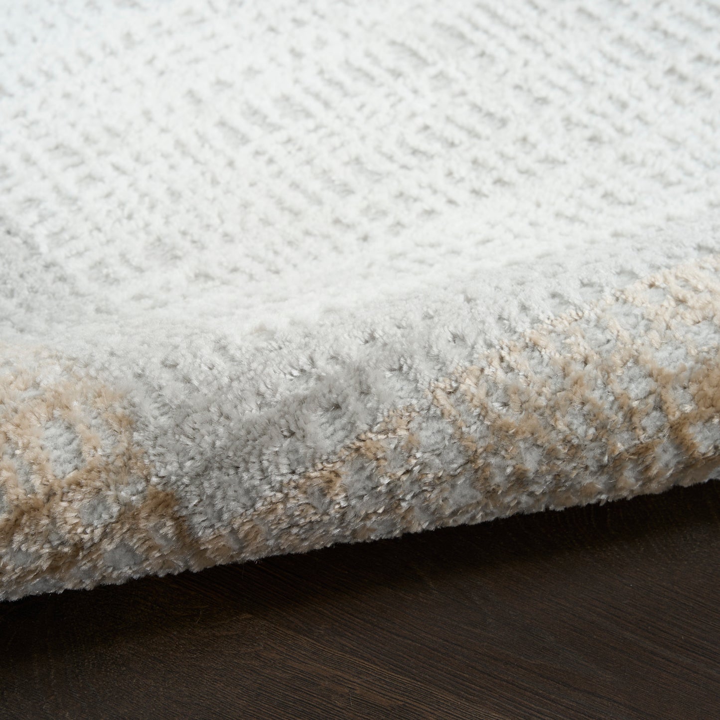 Cream and beige textured area rug with plush pile and subtle geometric pattern on dark wood floor.