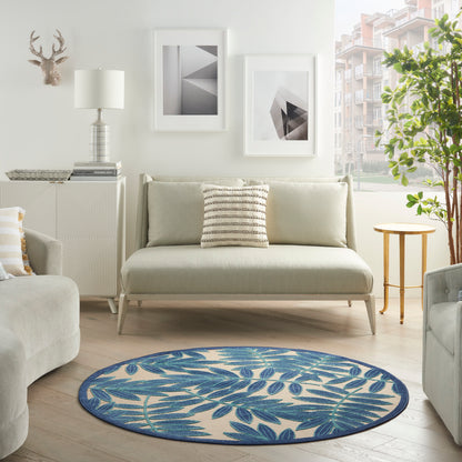 Round blue leaf-pattern rug on light wood floor in a modern neutral living room with beige sofa and white furniture.