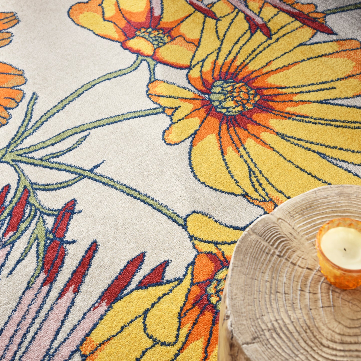 Close-up of floral rug with bright yellow-orange flowers, green stems on cream background, plus wooden candle tray.