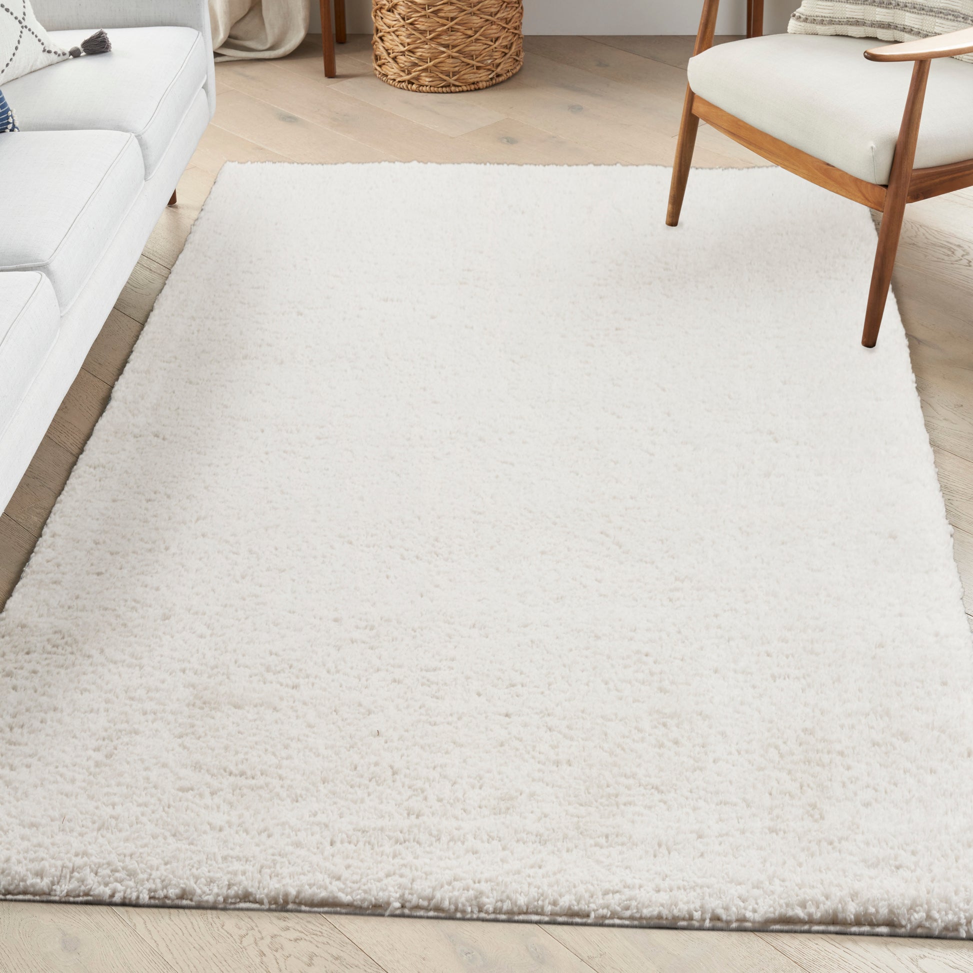 Cream plush shag rug in a bright living room with light wood floors, white sofa, and mid-century chair.