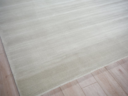 Cream beige flat-weave rug with soft texture on light wood floor; minimalist home decor.