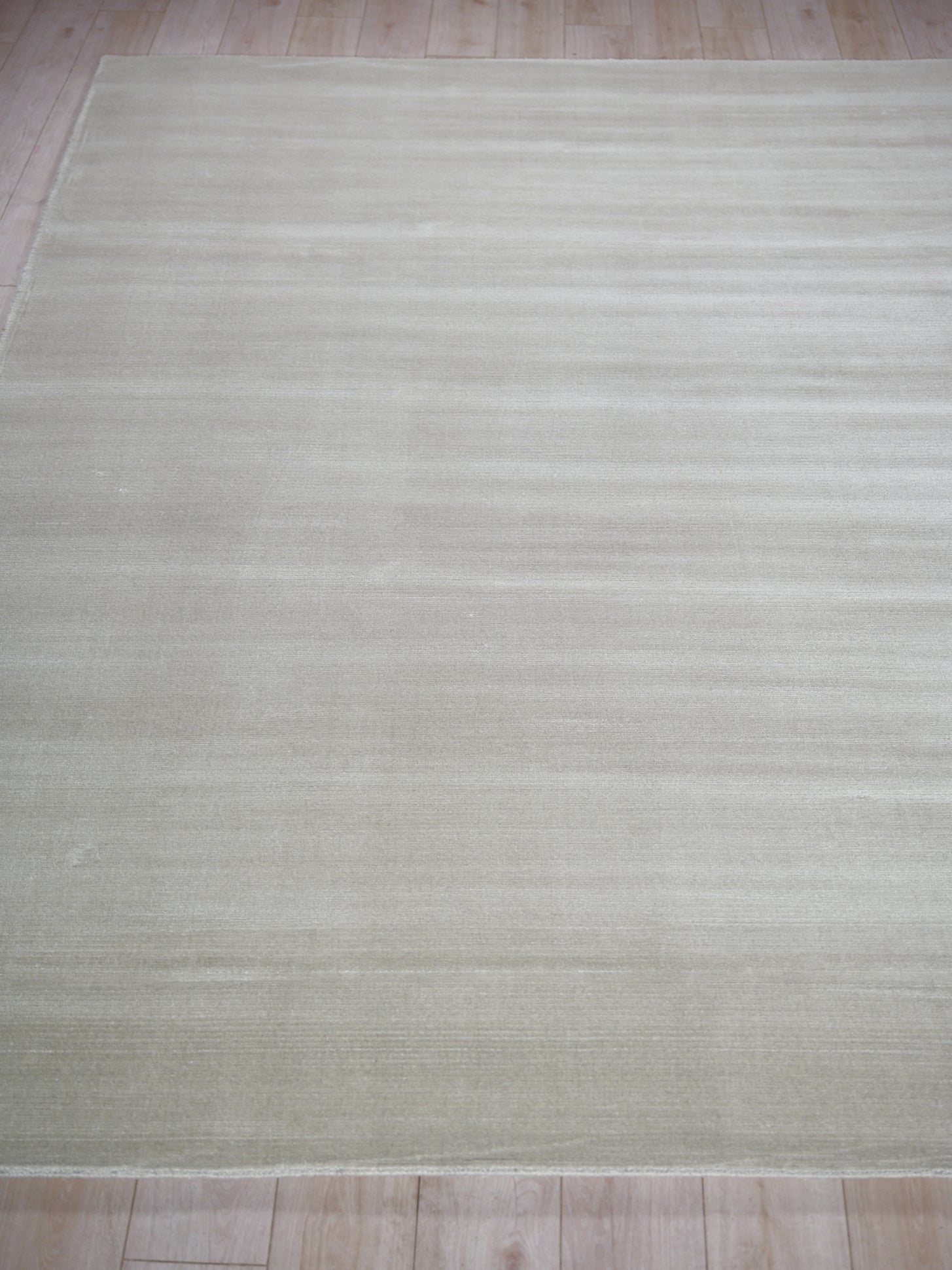 Light beige flatweave rug with subtle tonal stripes on a light wood floor