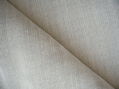 Beige ribbed upholstery fabric with fine vertical lines, folded diagonally, soft and versatile for sofas or cushions.