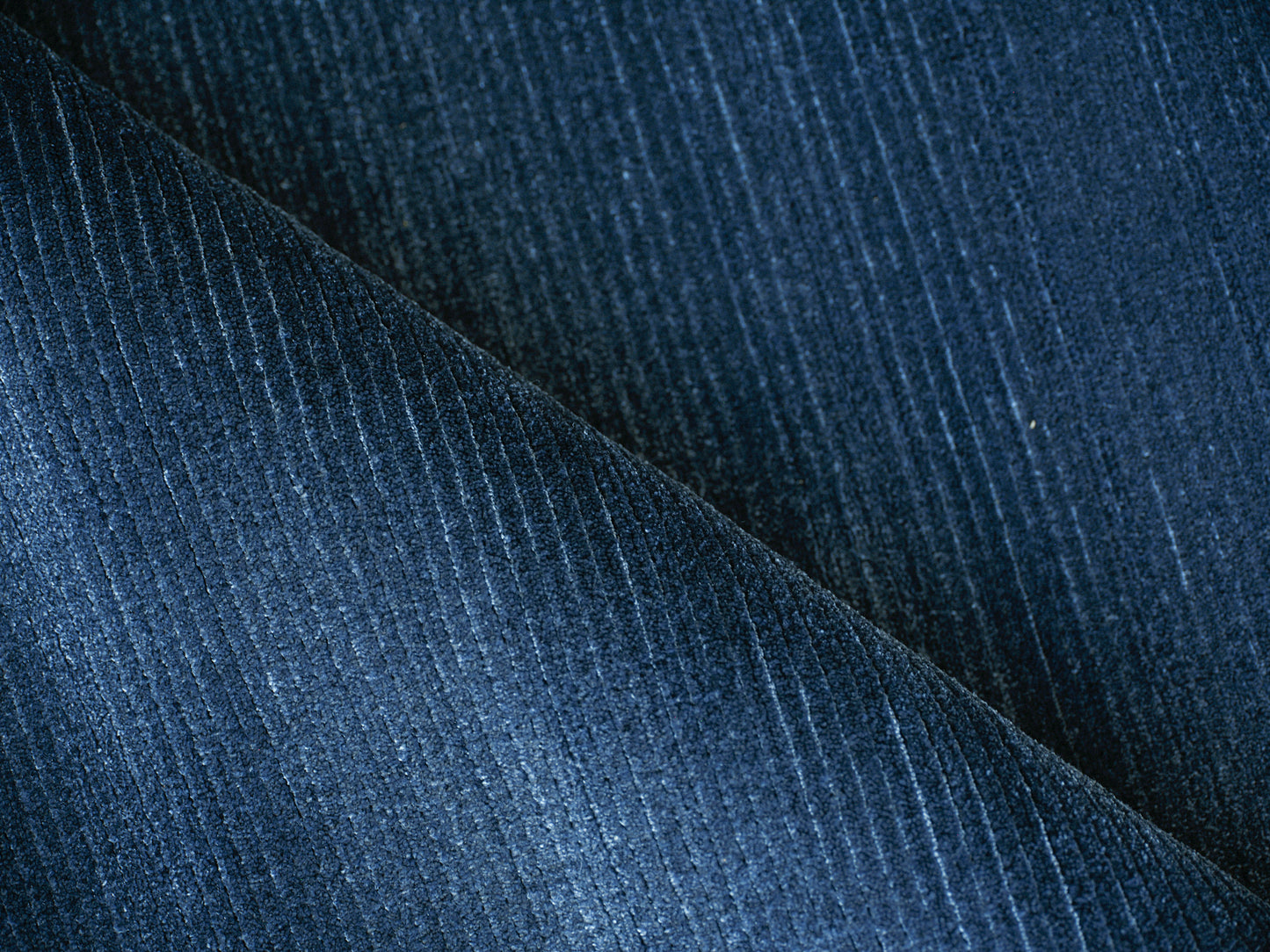Dark blue corduroy fabric close-up with vertical wales, folded diagonally.