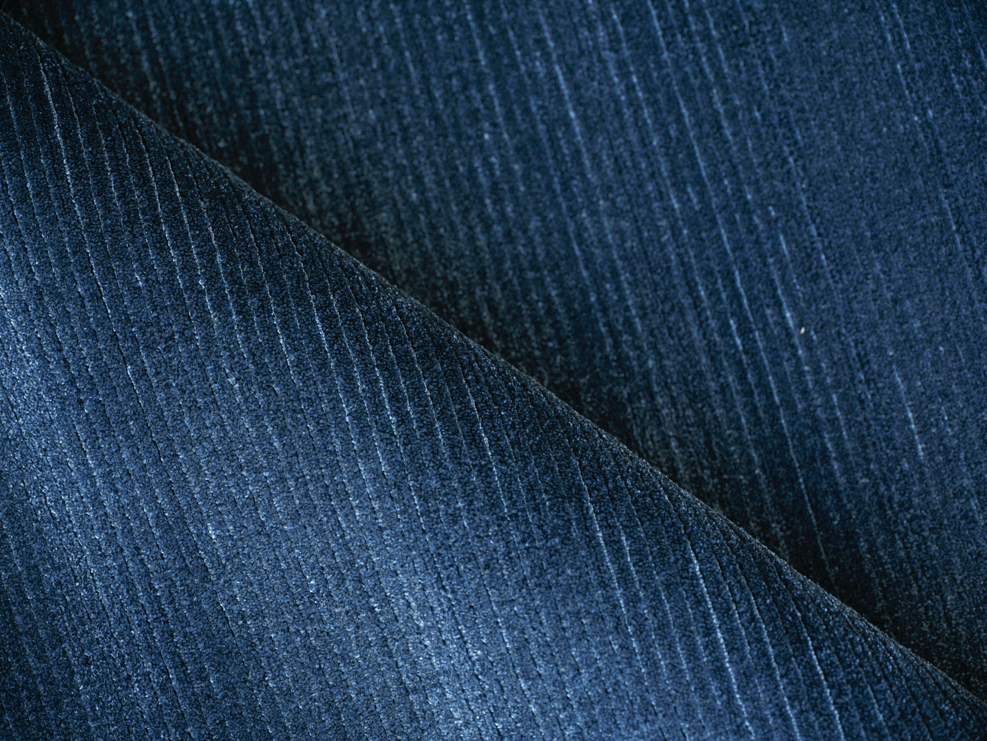 Dark blue corduroy fabric close-up with vertical wales, folded diagonally.