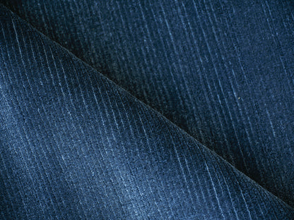 Dark blue corduroy fabric close-up with vertical wales, folded diagonally.