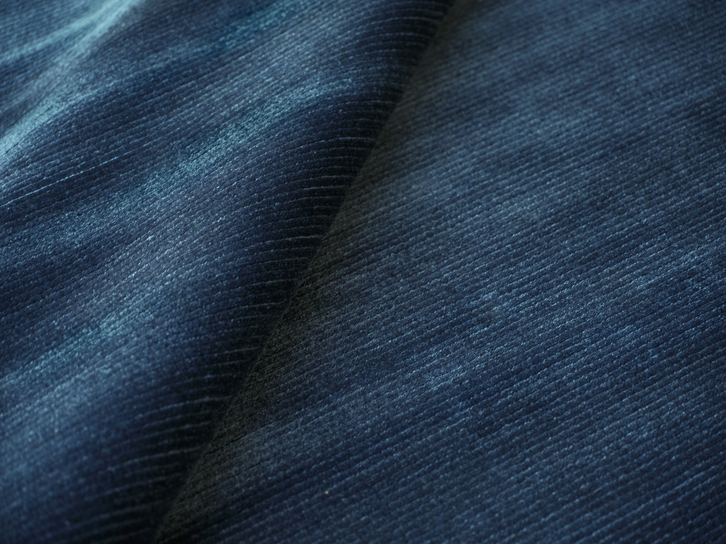 Close-up of dark blue denim fabric showing tight twill weave and soft folds.
