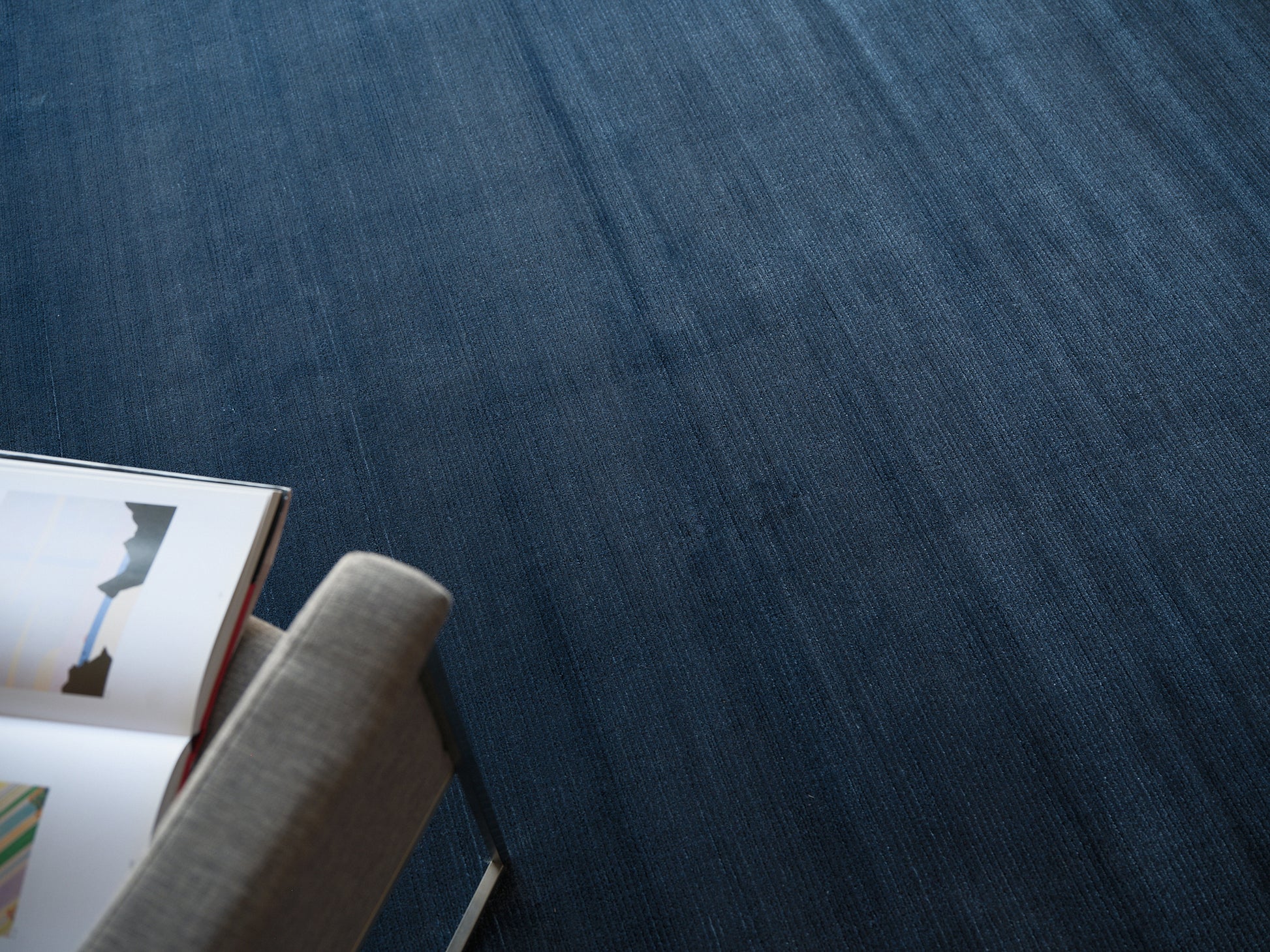 Blue textured rug with a light gray upholstered chair at the edge and an open magazine on the seat.