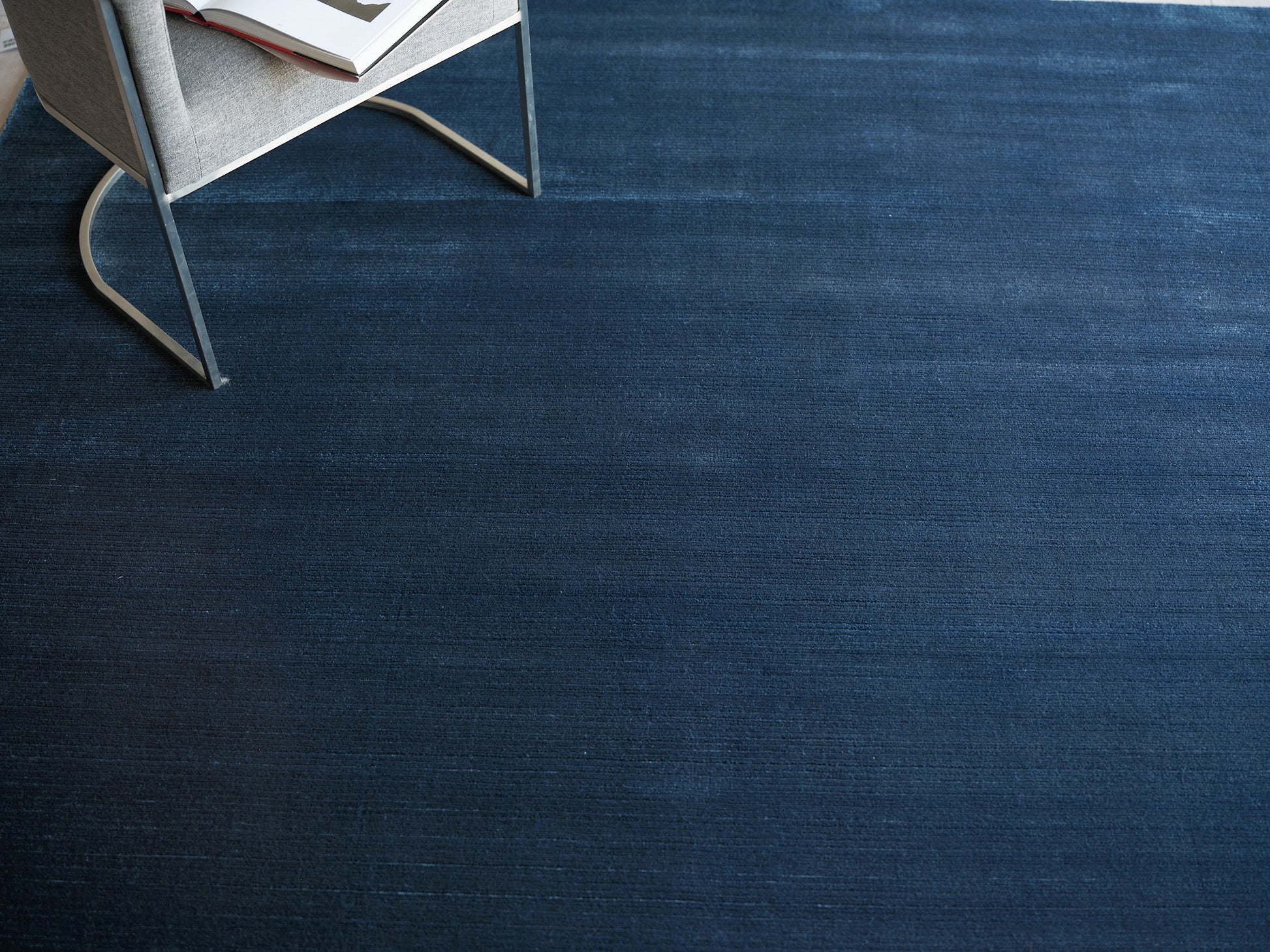 Blue textured rug with a gray upholstered chair and an open book resting on its seat.