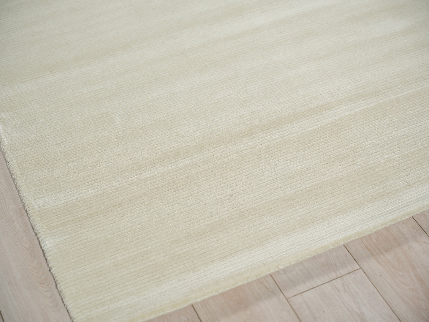 Cream rectangular area rug with a soft ribbed texture on a light wood floor.