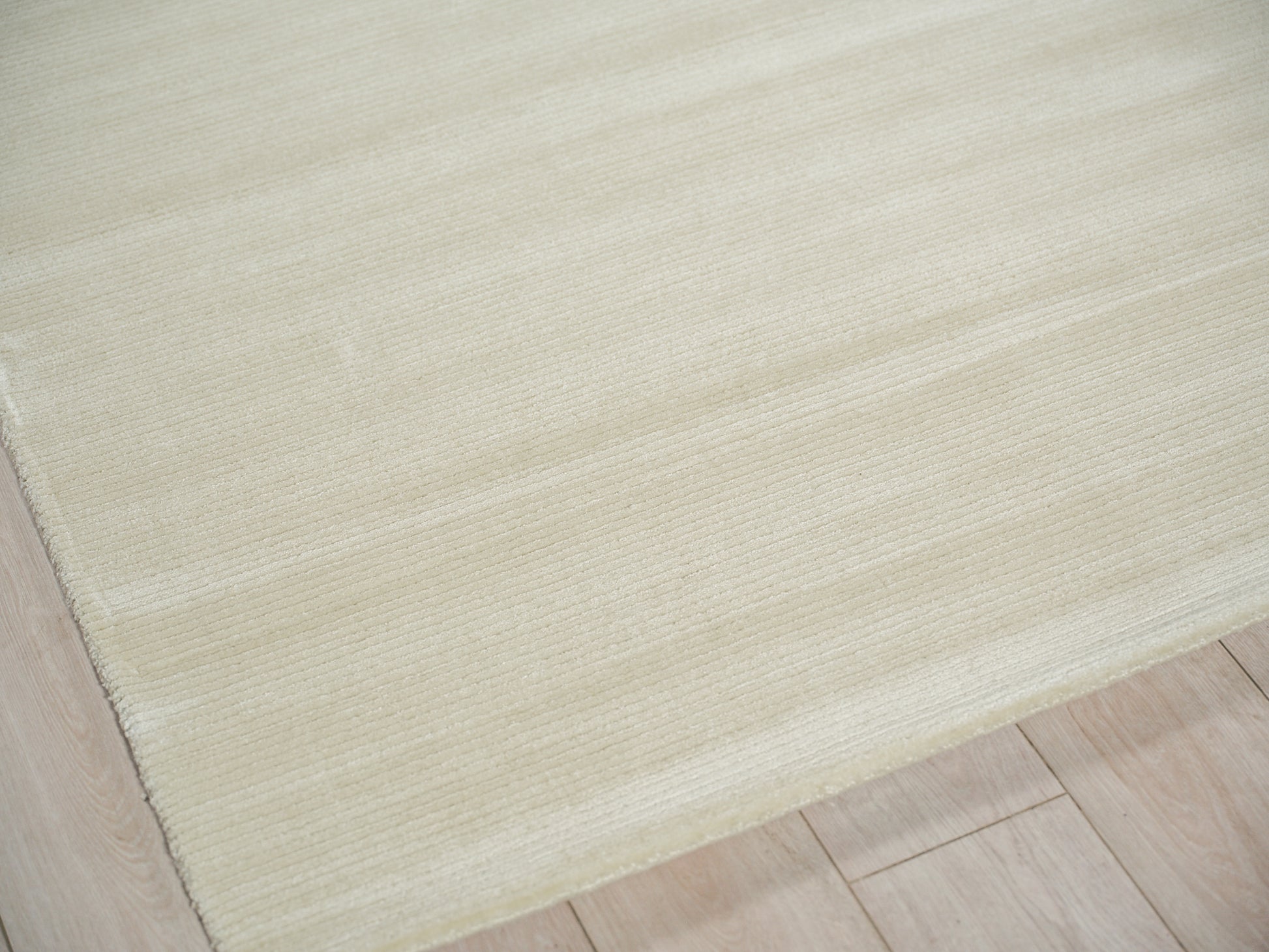 Beige rectangular rug with a soft low-pile texture and subtle horizontal stripes on light wooden floor.