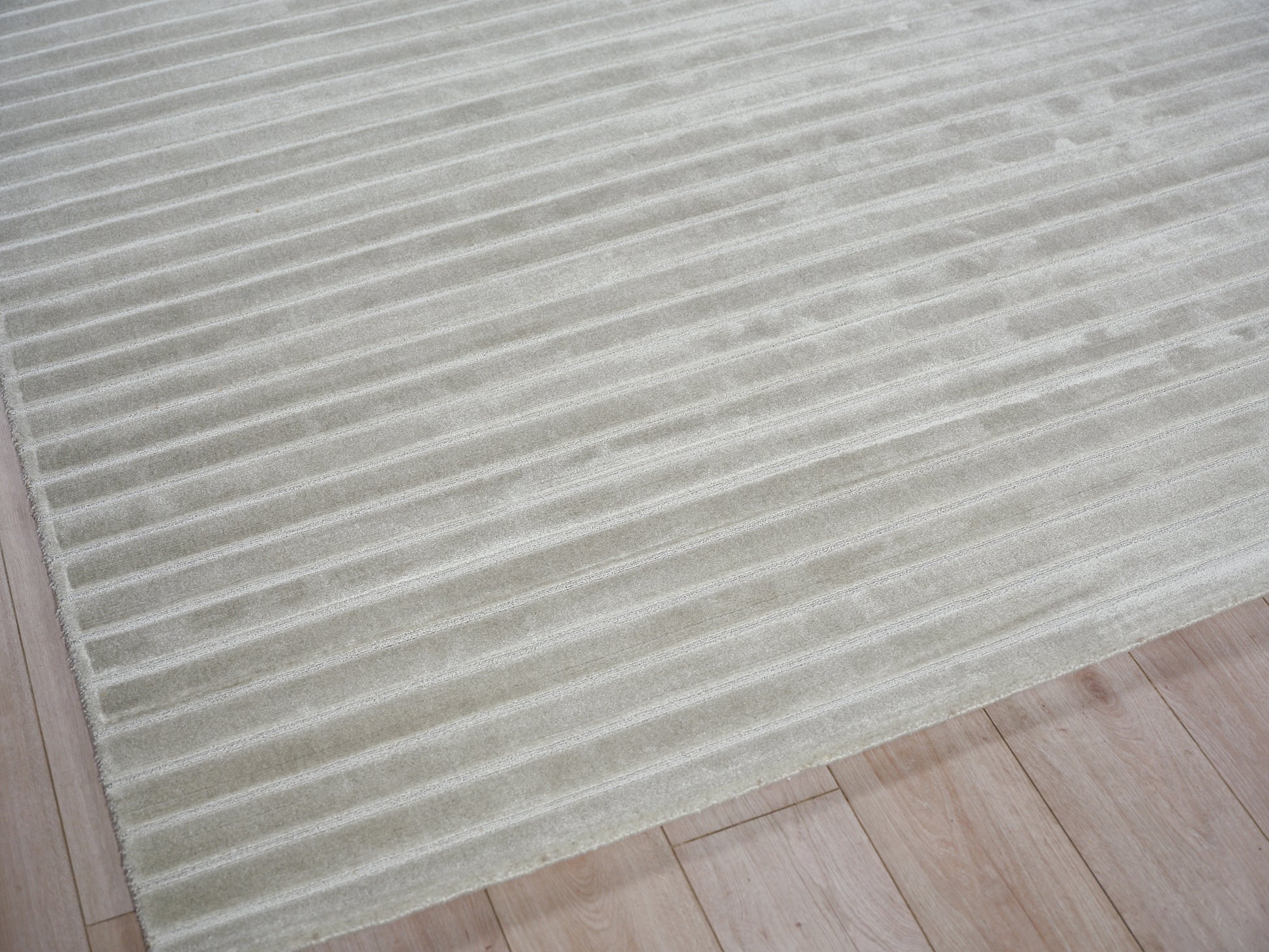 Creamy beige rug with uniform ribbed stripes on a light wood floor.