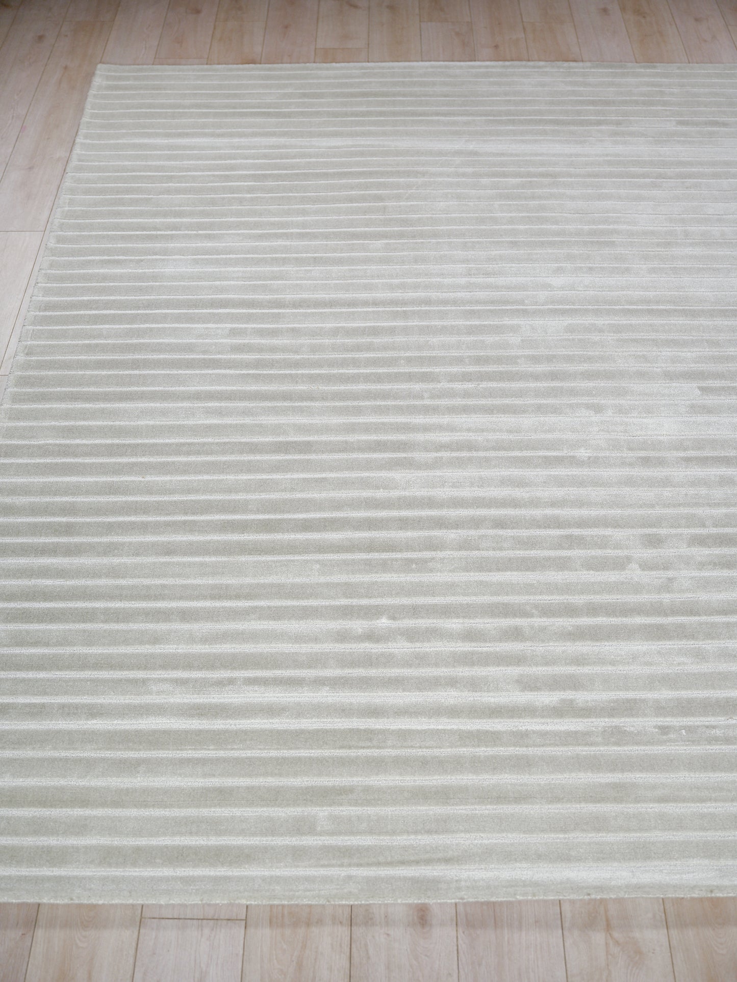 Light gray area rug with subtle horizontal stripes and plush texture on a light wood floor.