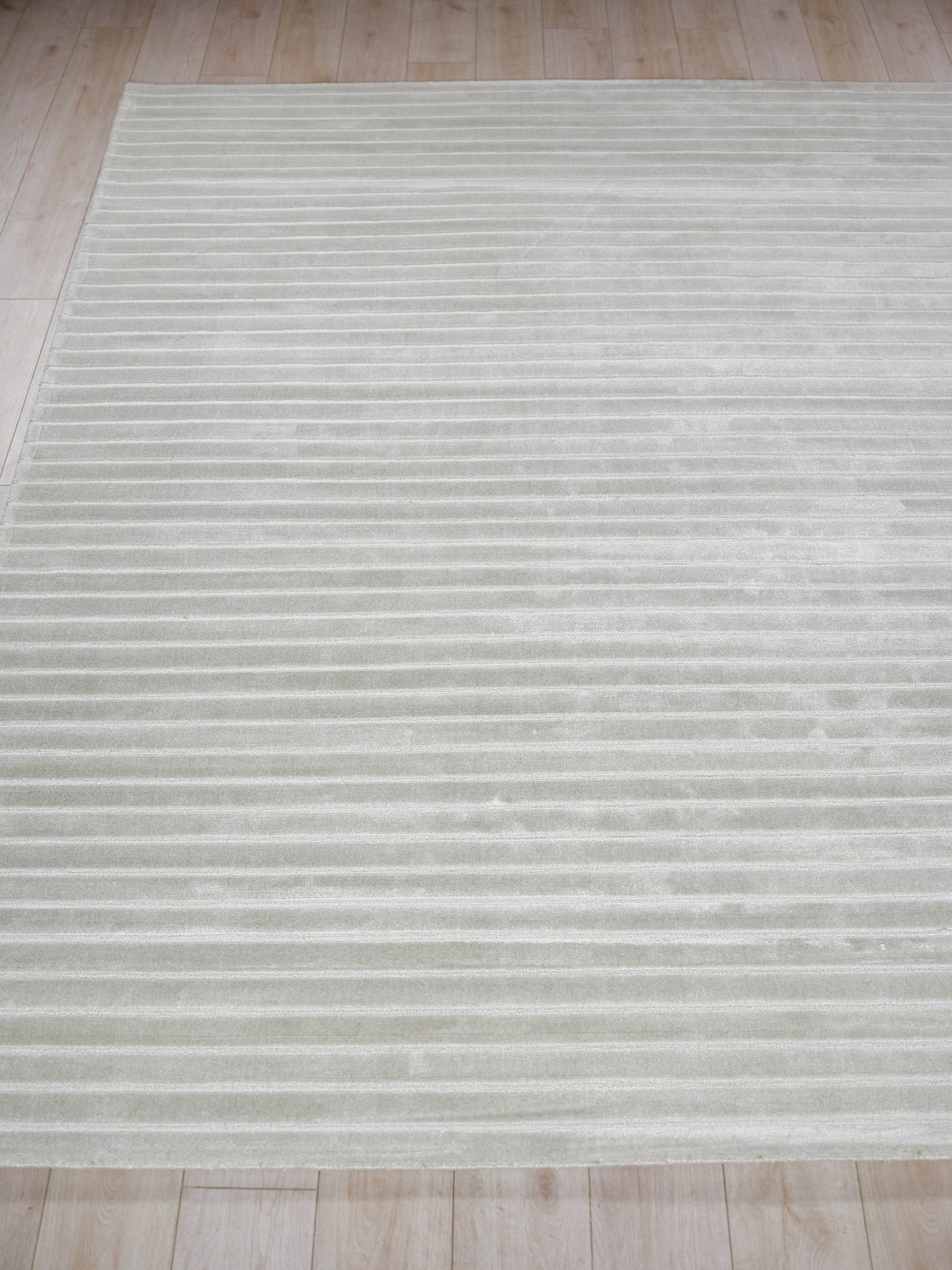 Light gray area rug with subtle horizontal stripes and plush texture on a light wood floor.
