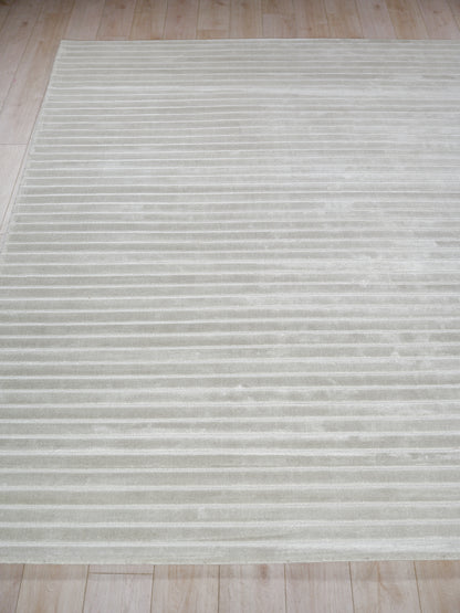 Light gray area rug with subtle horizontal stripes and plush texture on a light wood floor.