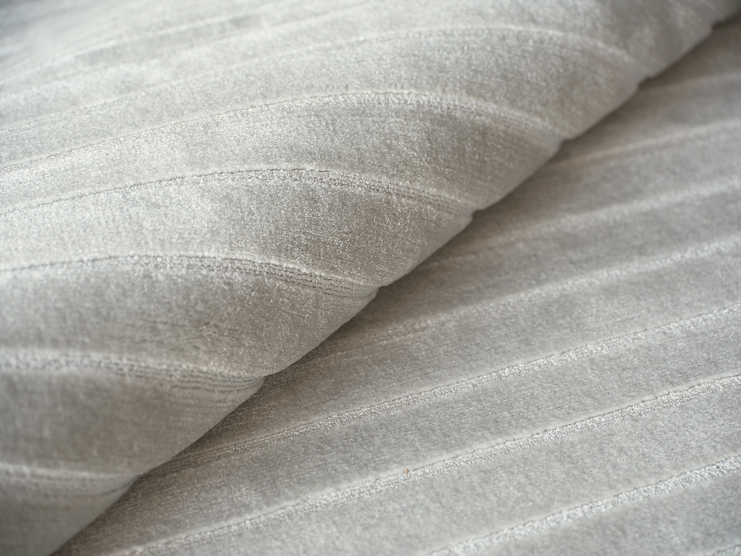 Close-up of pale gray hand-loomed rug fibers with a soft ribbed texture and gentle folds.