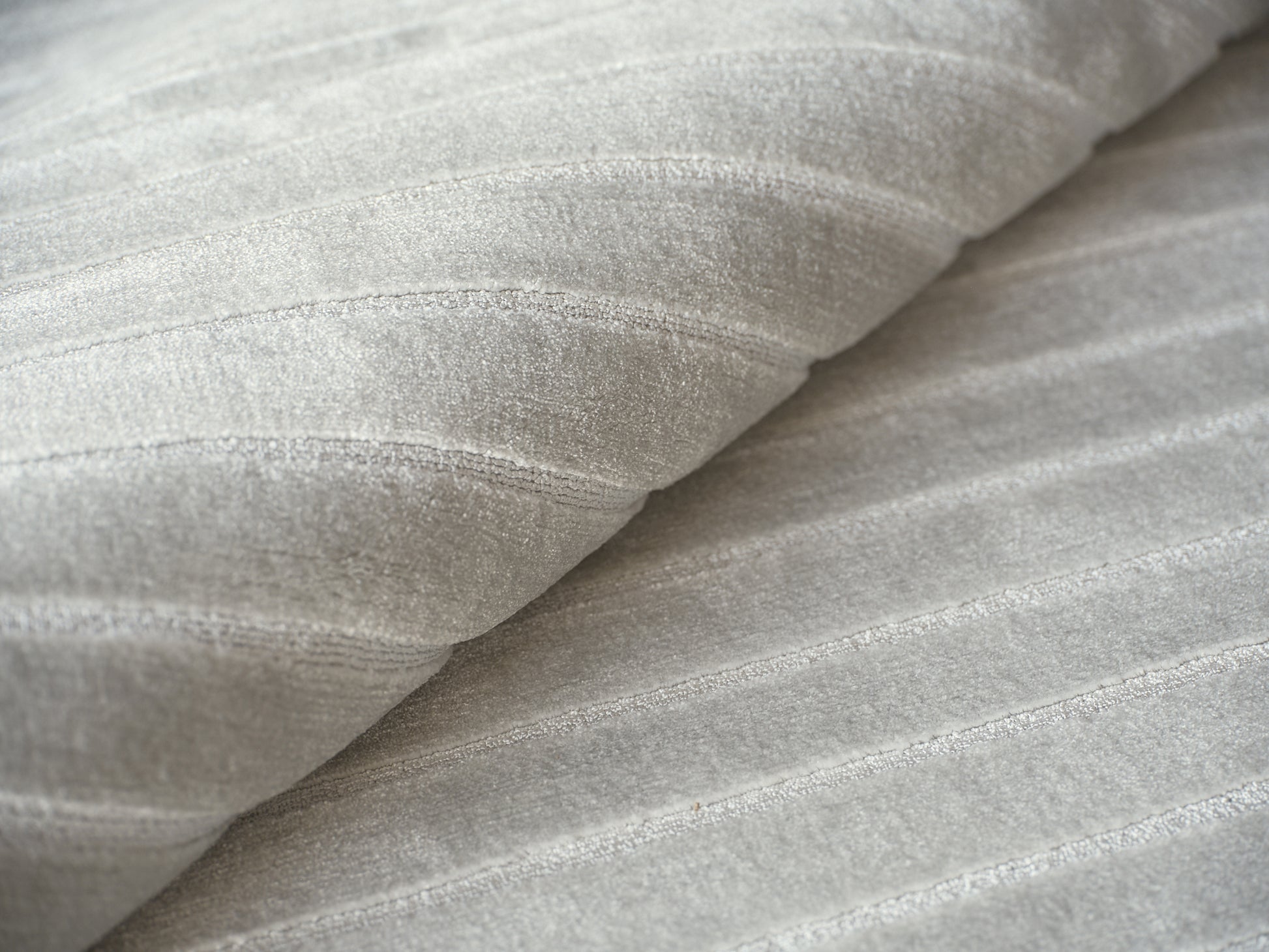 Close-up of pale gray hand-loomed rug fibers with a soft ribbed texture and gentle folds.