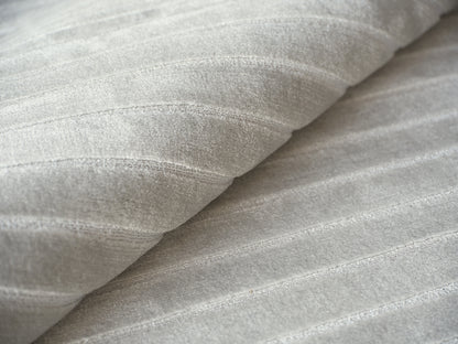 Close-up of pale gray hand-loomed rug fibers with a soft ribbed texture and gentle folds.
