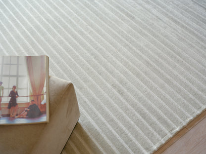 Light gray striped textured rug with diagonal ridges, beige sofa corner & a photo book resting on its edge.