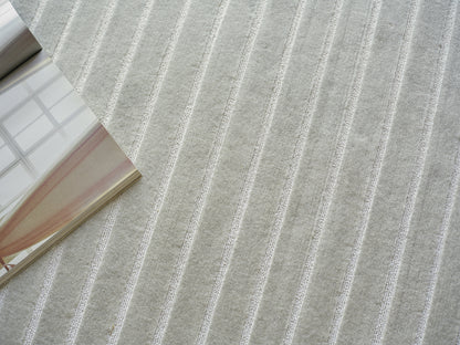 Light gray striped area rug with raised white lines; soft modern texture, magazine resting on left edge