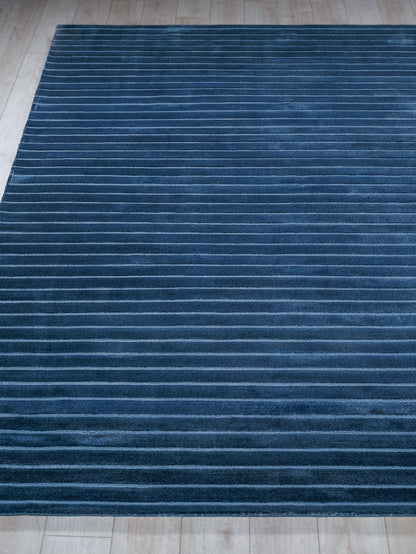 Dark blue plush rug with thin light-blue horizontal stripes on a wooden floor.