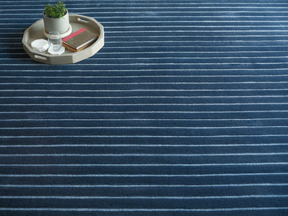 Round light wood tray on a dark blue striped rug, with a potted plant, glass, coasters and notebooks.