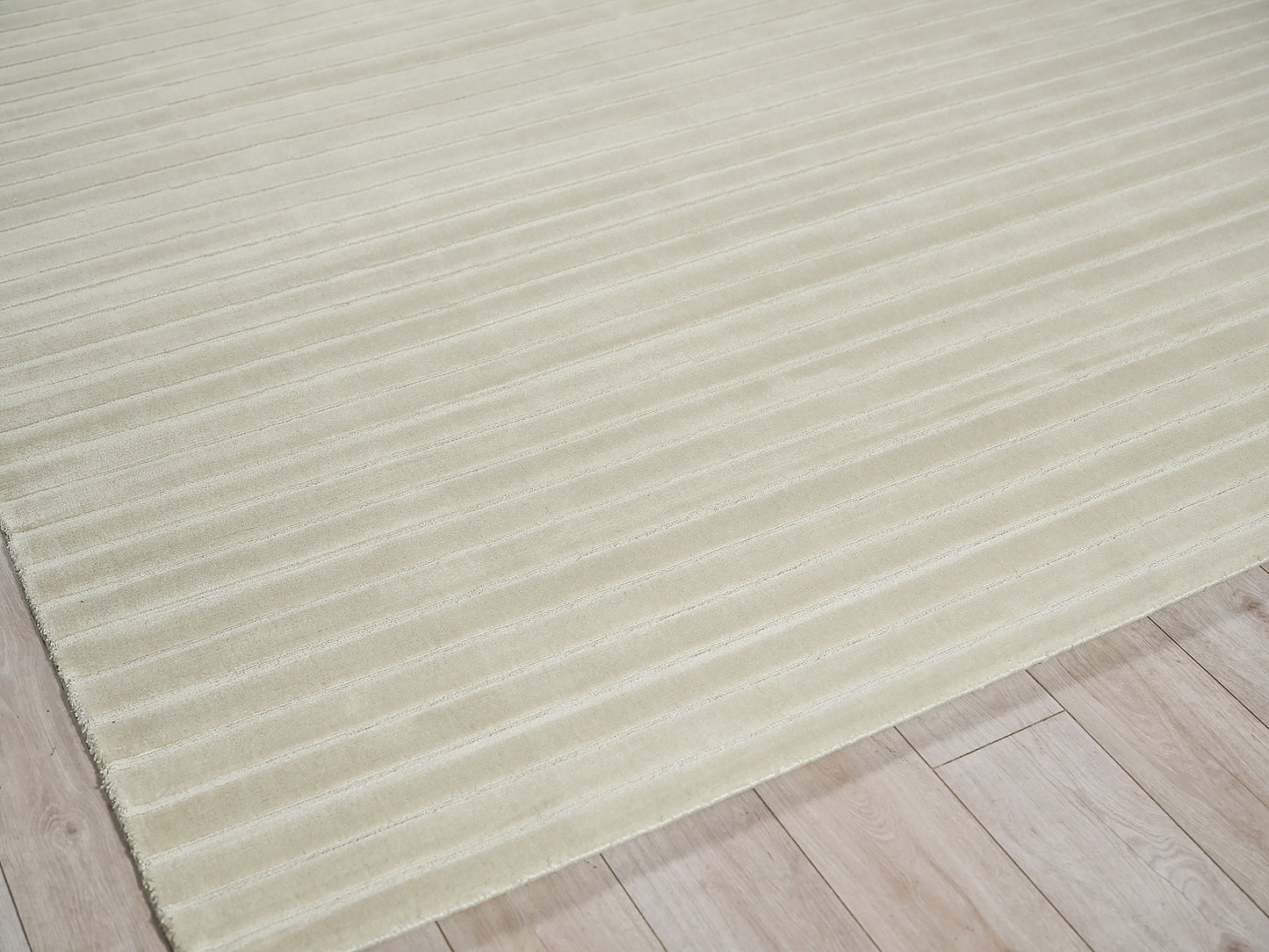 Beige ribbed area rug, low-pile with horizontal grooves, laid on light wood flooring.