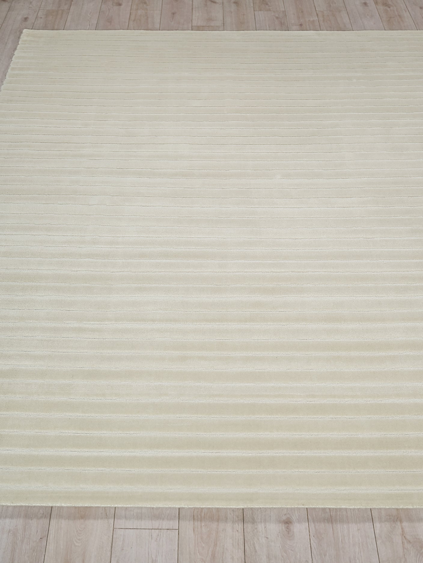 Cream flat-weave rug with subtle horizontal stripes on a light wooden floor.