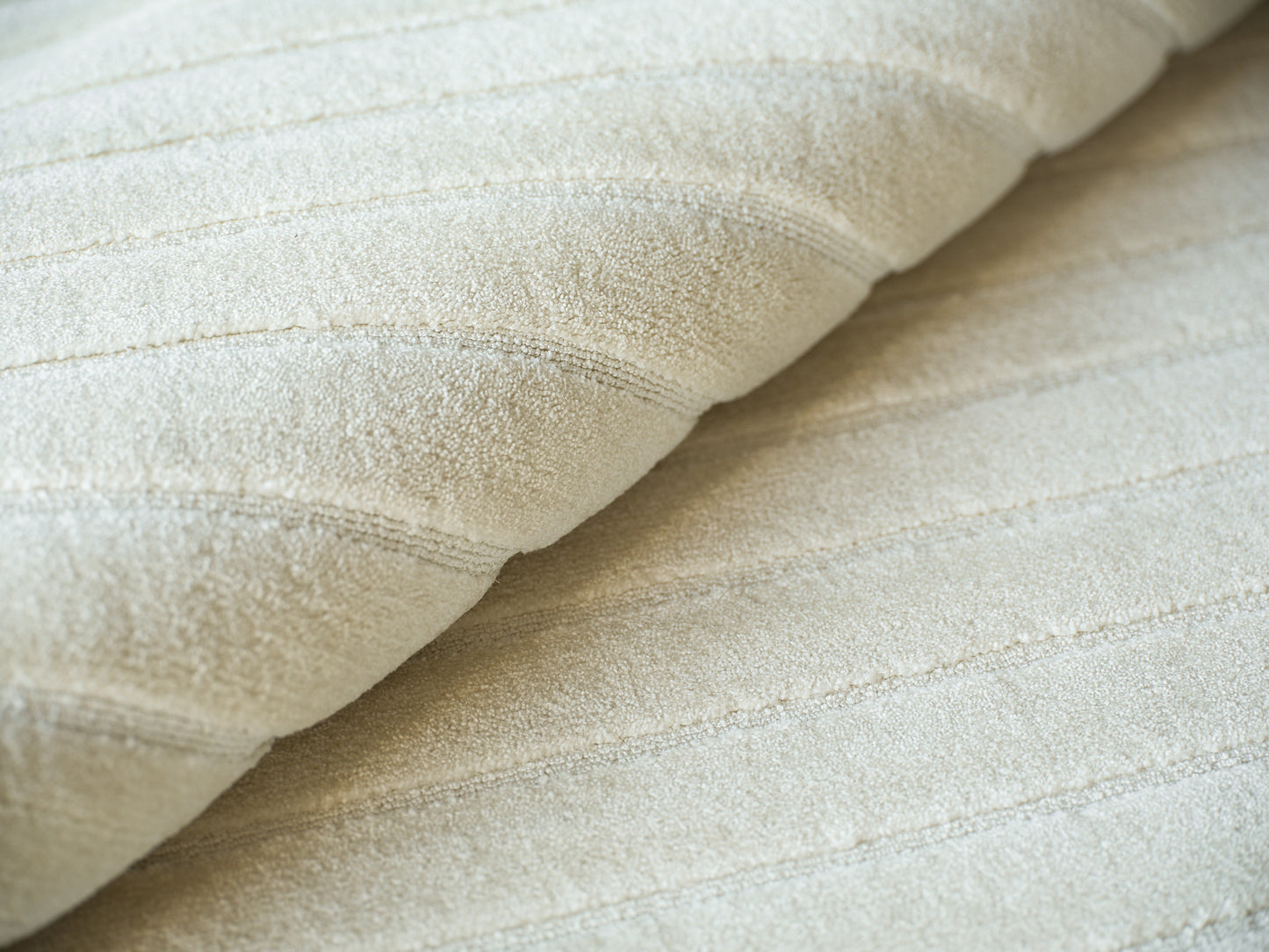 Cream beige hand loomed rug with subtle stitched stripes, folded for display, 2' x 3'.