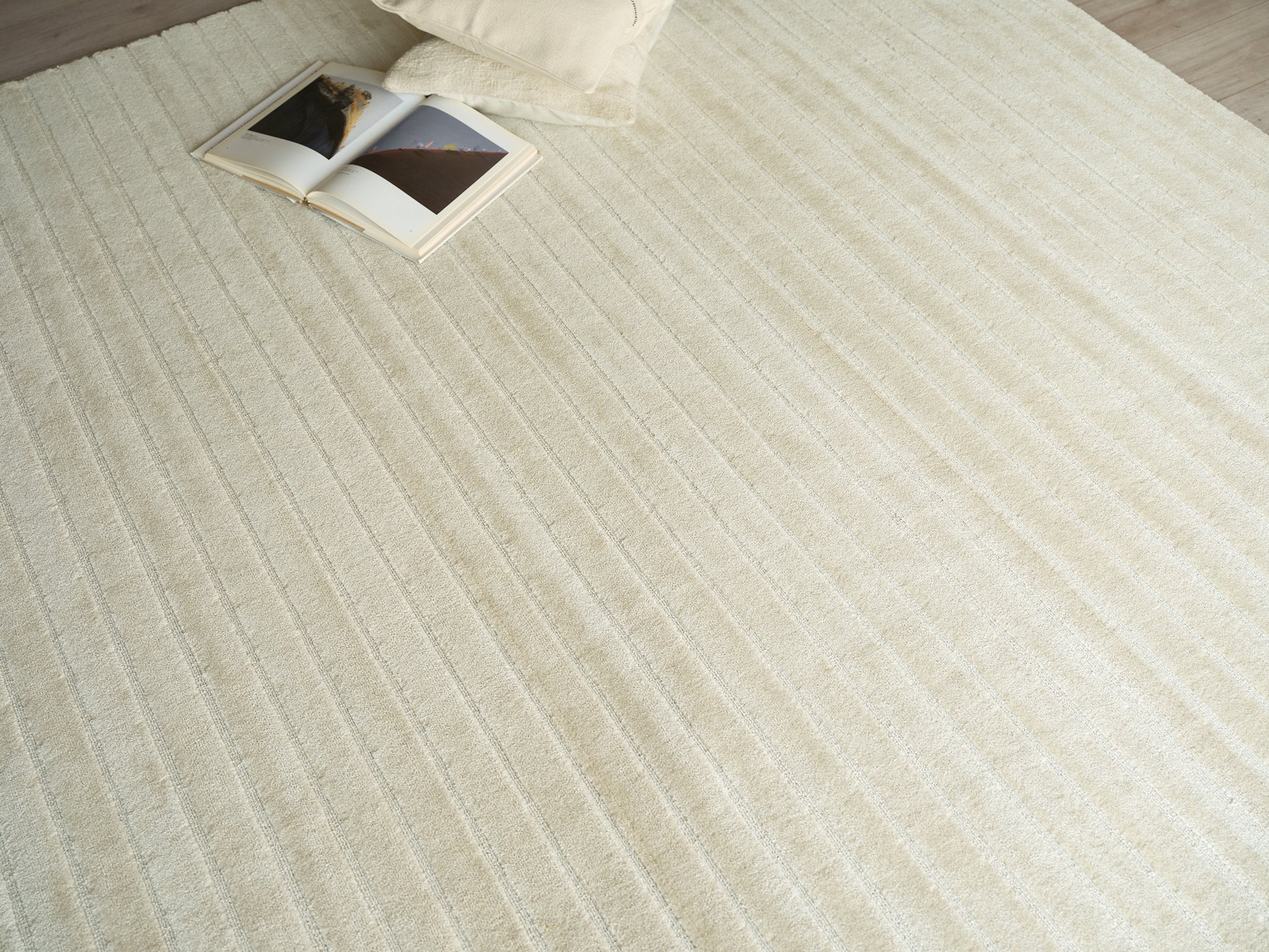 Cream textured rug with parallel stripes; open magazine and a pale pillow at the corner.