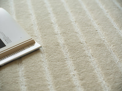 Beige striped textured rug with soft pile; open magazine resting on left edge, cozy home scene.