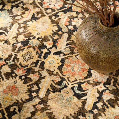 Handwoven oriental rug with geometric motifs in cream, brown, tan, blue and orange; round ceramic vase with dried branches.