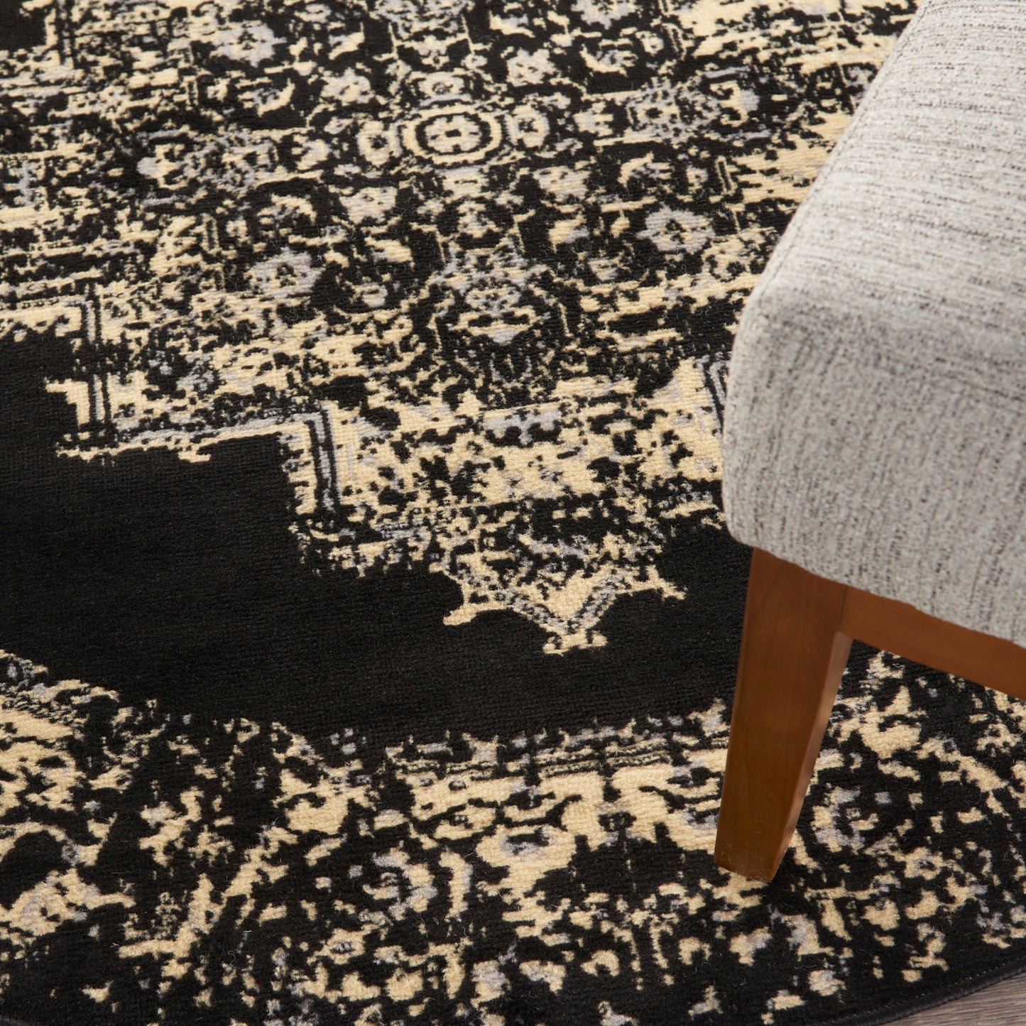 Black and beige distressed oriental rug with cream highlights under a gray upholstered chair with a wooden leg.