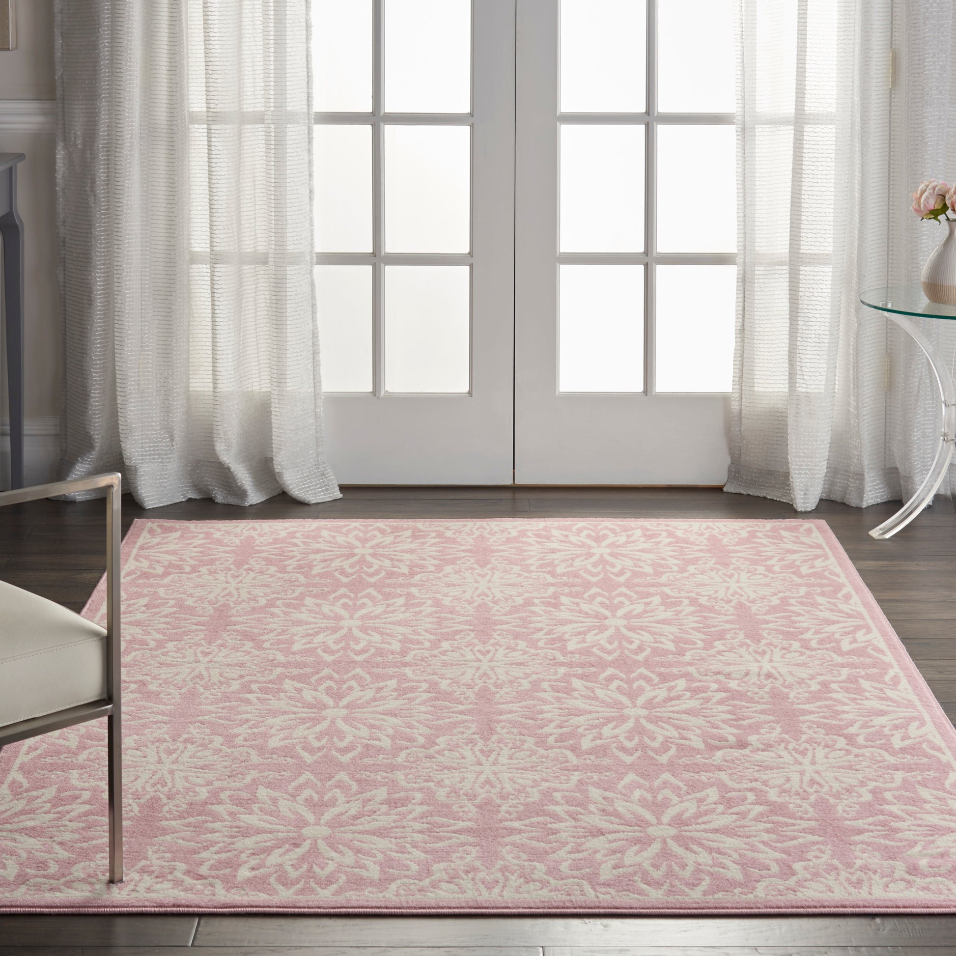Rectangular pink damask-pattern rug on dark wood floor in a bright living room with sheer curtains.