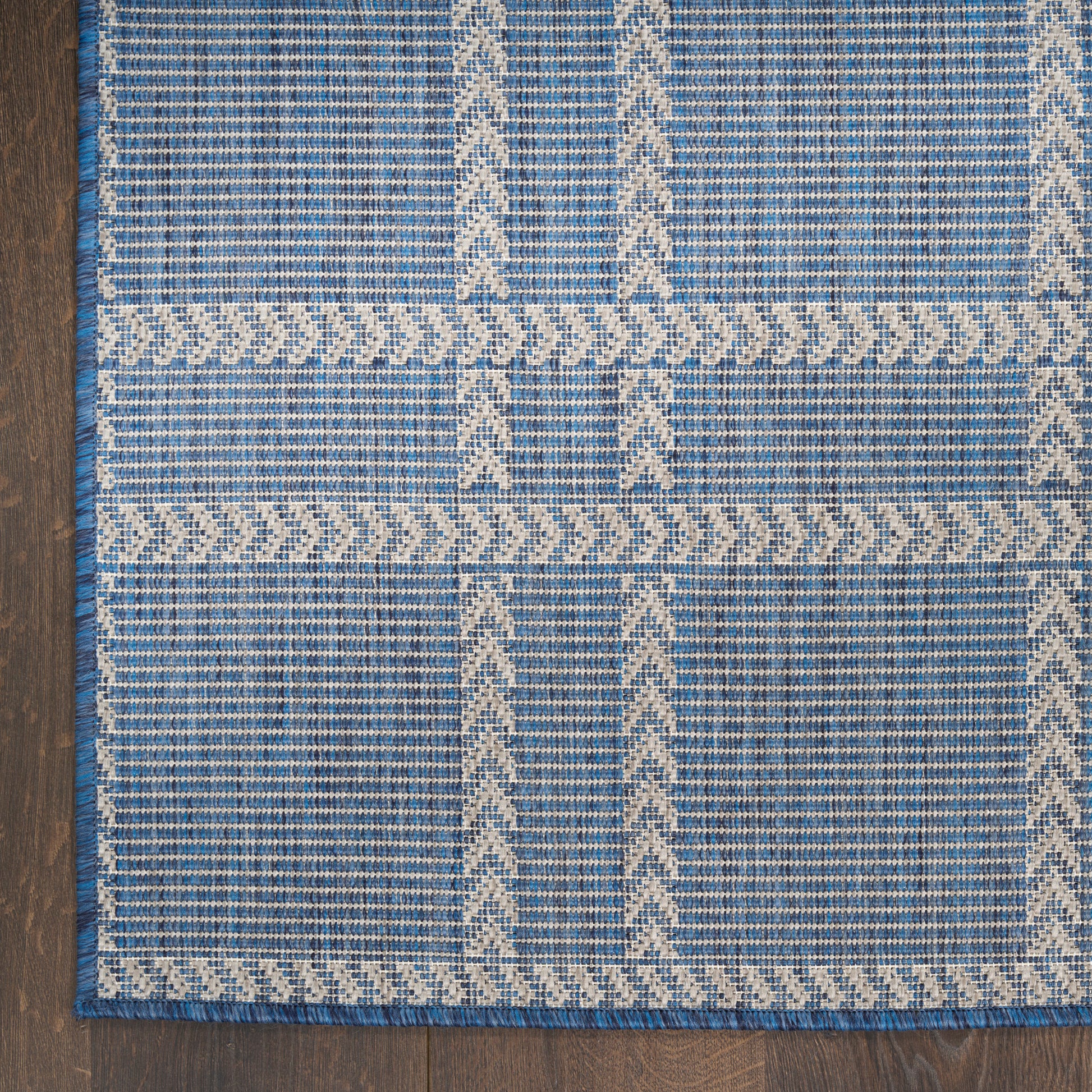 Blue flat-weave rug with cream geometric patterns and a braided border; rectangular, rustic boho style.