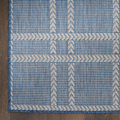 Blue flat-weave rug with cream geometric patterns and a braided border; rectangular, rustic boho style.