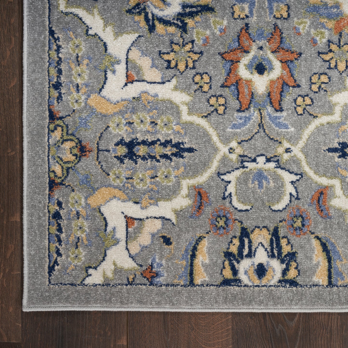 Traditional oriental-style area rug with blue, cream, orange and yellow floral motifs on gray; light border on wood floor.