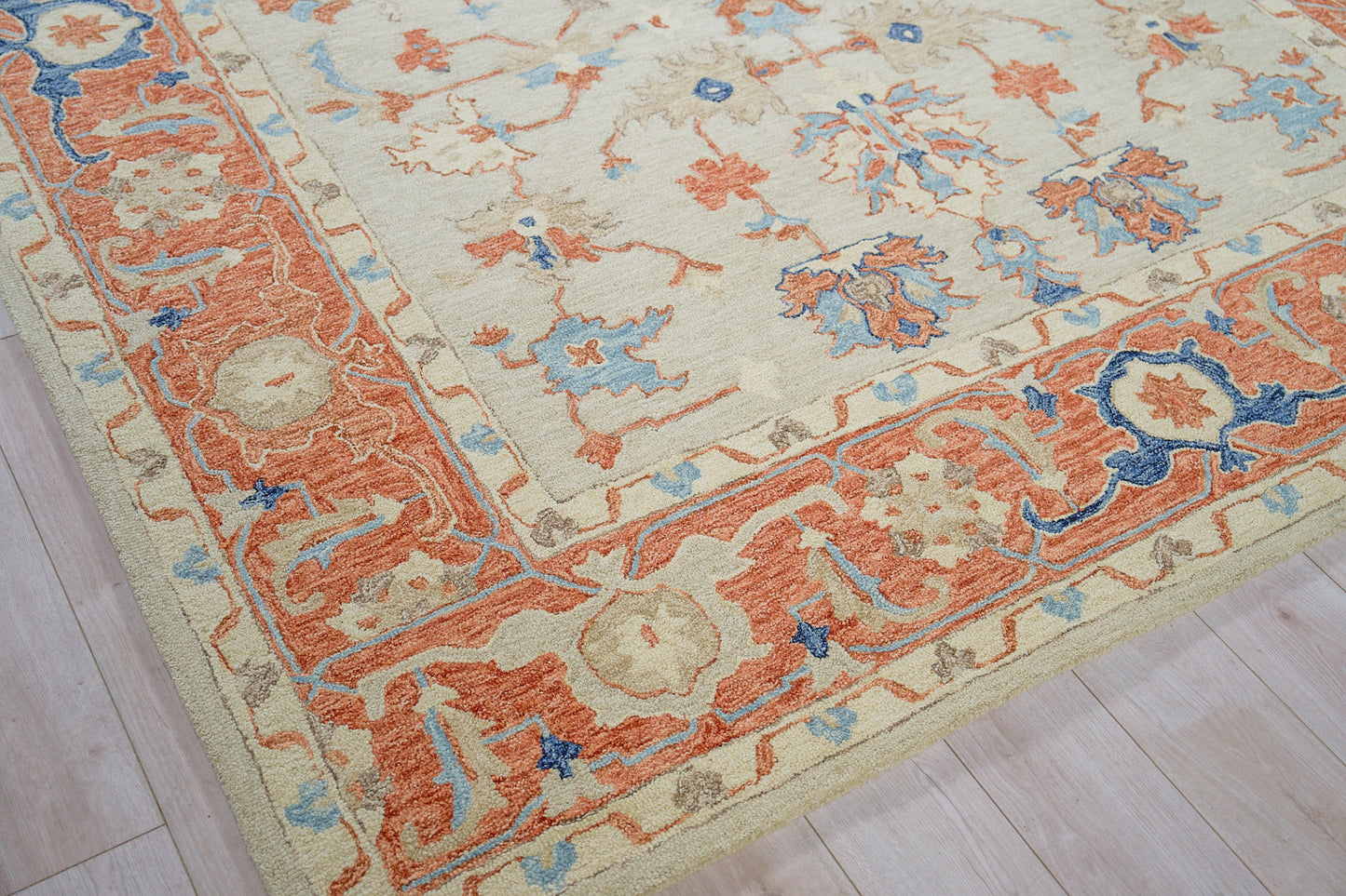 Traditional Persian-style area rug with cream field, orange border and blue floral accents on a light wood floor.