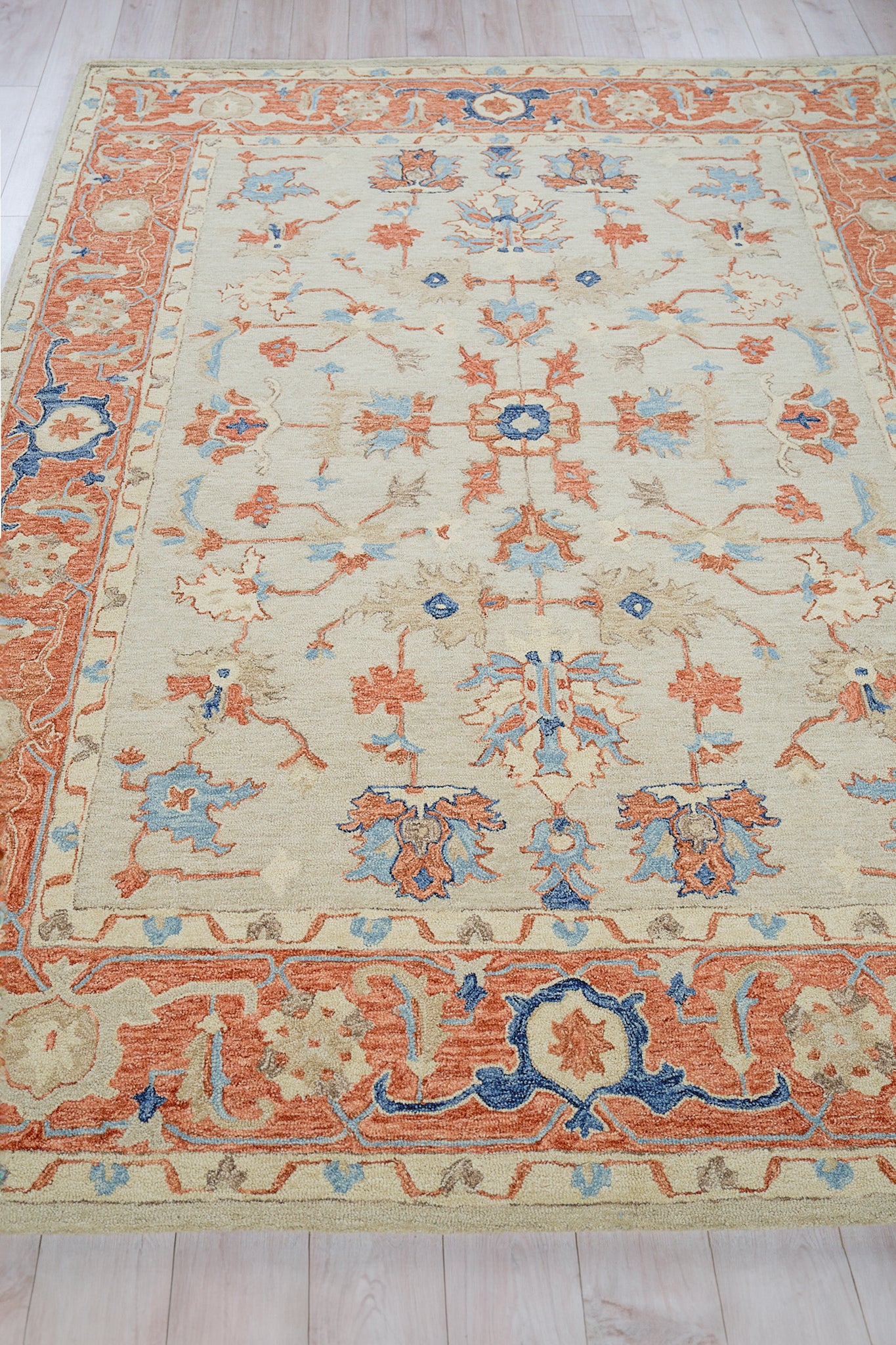 Rectangular oriental-style area rug with cream field, blue and orange floral motifs, and a rust-orange border.