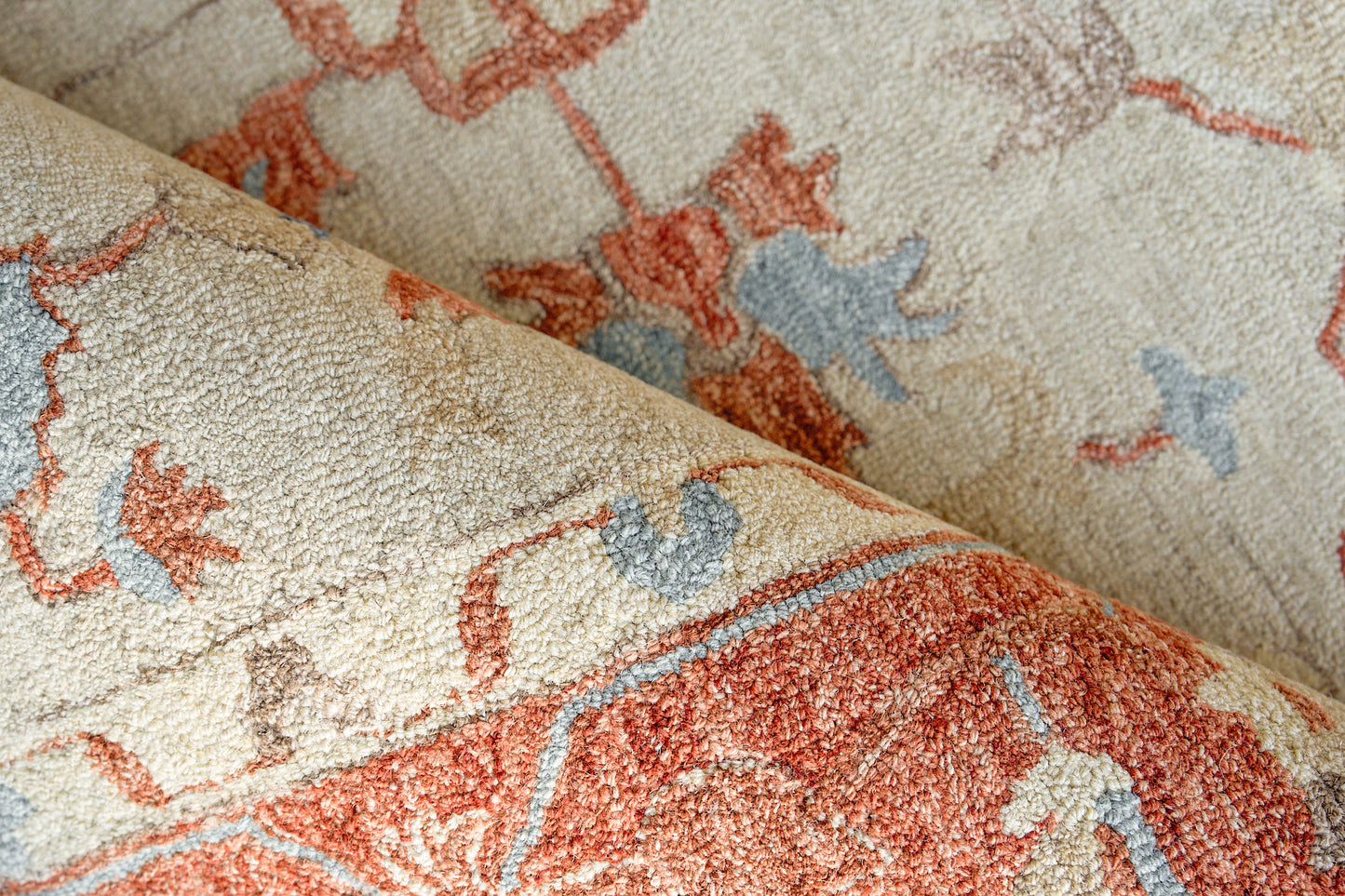 Close-up of a textured beige rug with coral pink and light blue floral motifs; rolled hand-tufted rug.