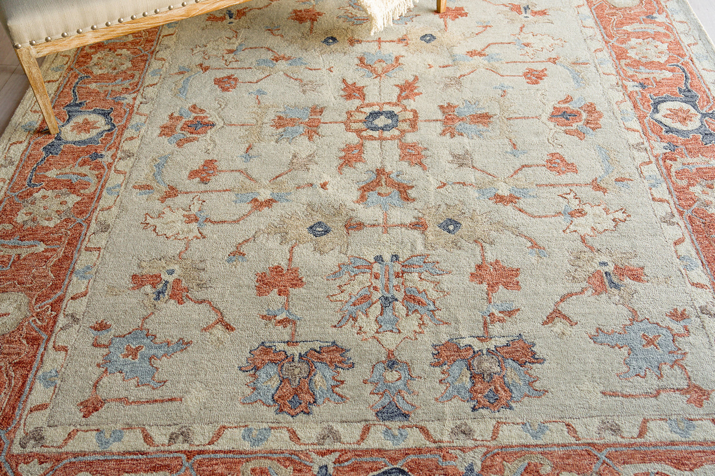 Beige Persian-style area rug with red and blue floral motifs, ornate border and fringed edges.