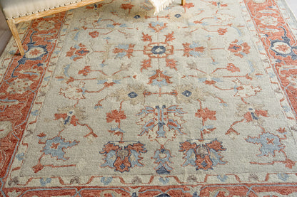 Beige Persian-style area rug with red and blue floral motifs, ornate border and fringed edges.
