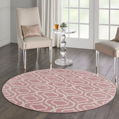 Round pink rug with white loop pattern, beige upholstered chairs with metal legs, glass side table with plant and drink.