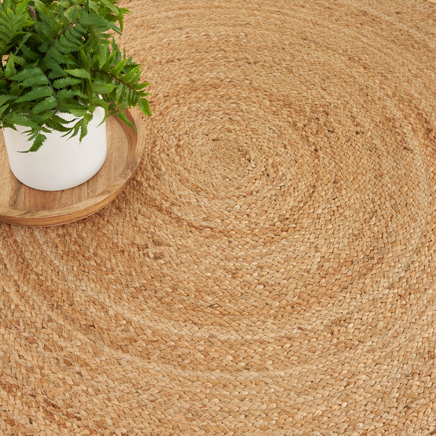 Natural round jute rug with a fern in a white pot on a wooden tray, boho decor.