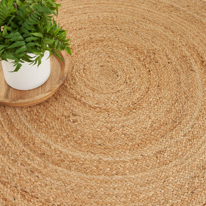 Natural round jute rug with a fern in a white pot on a wooden tray, boho decor.