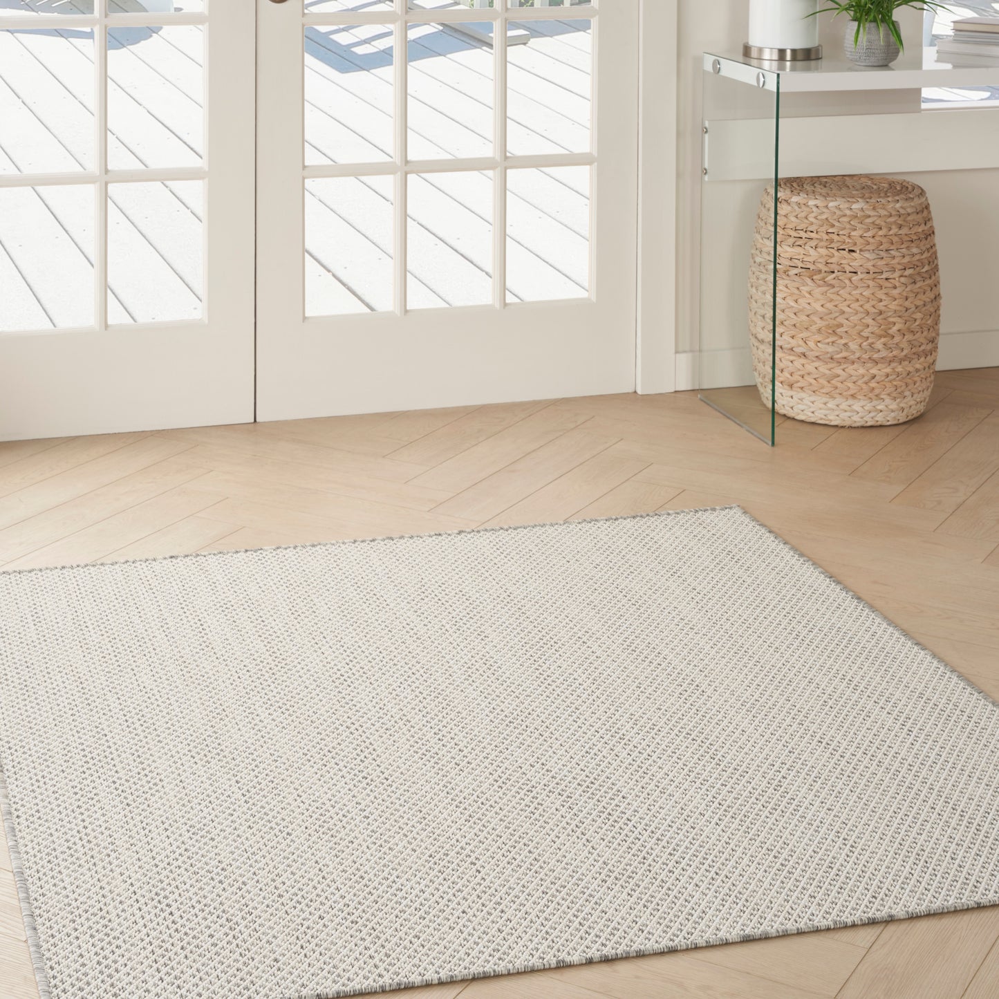 Cream textured rectangular rug on light wood entryway floor, with wicker basket & glass console nearby.